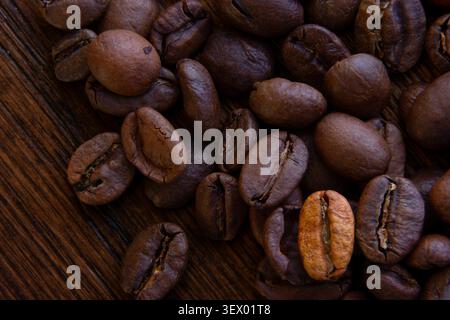 Nahaufnahme von gerösteten Kaffeebohnen, die über eine rustikale Holzoberfläche verstreut sind und eine leichte geröstete Bohne für visuelle Kontraste sorgen Stockfoto