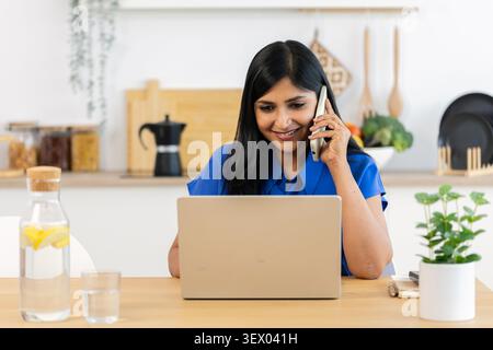 Indische Frau, die mit dem Smartphone spricht, während sie aus der Ferne arbeitet Stockfoto