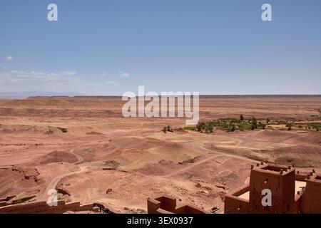 Der weite, trockene Wüstenhorizont, der die Provinz Ouarzazate in Marokko umgibt, erstreckt sich majestätisch unter einem blauen Himmel, der von schroffen Wolken gesäumt ist Stockfoto