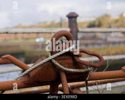 Eine Nahaufnahme konzentriert sich auf einen stark verrosteten Anker, der mit dickem Seil gesichert ist und als mächtiges Symbol für maritime Geschichte und Ausdauer dient. Das flache Stockfoto