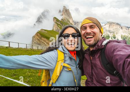 Fröhliches Paar von Wanderfreunden, die Selfie in den Dolomiten machen. Millennial Guy Girl genießt Sommerausflüge und lacht vor der Kamera zusammen Stockfoto