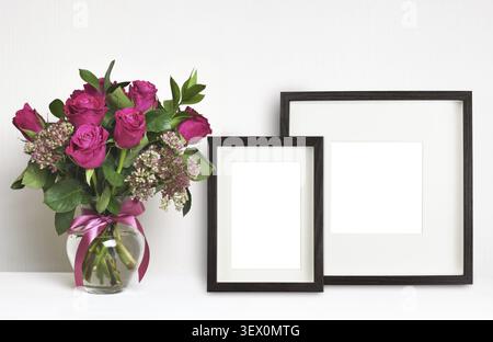 Strauß aus rosa Rosenblüten in einer Glasvase und braunen leeren Rahmen auf weißem Hintergrund. Mock-Up Stockfoto