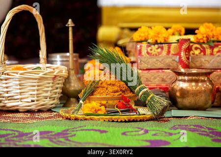 Eine Nahaufnahme eines goldenen Tellers mit heiligen Gegenständen wie Kurkumapulver, Ringelblume und Grasbündeln, die in hinduistischen Ritualen verwendet werden Stockfoto