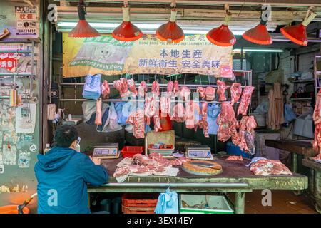 Traditioneller Metzgerstand auf einem feuchten Markt in Hongkong. Es enthält verschiedene Stücke von frischem Schweinefleisch auf Haken und einen großen Holzhackblock Stockfoto