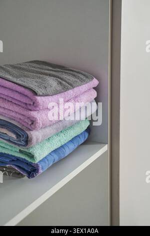 Gefaltete Handtücher Auf Offenem Regal Im Minimalen Schrank Mit Pastelllila Grünen Blauen Und Grauen Stoffen Mit Sichtbarer Textur Und Ordentlicher Organisation Im Innenraum. Stockfoto
