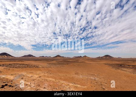 Eine entfernte Gestalt geht unter einem weiten Makrelenhimmel über vulkanischen Gipfeln, Wüste Schwarz, Ägypten Stockfoto