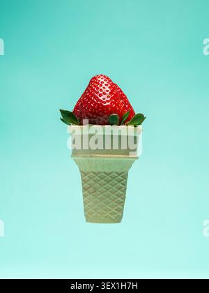 Minimales kreatives Lebensmittelkonzept mit einer frischen roten Erdbeere, die in einer Waffeleiskegel auf weichem blauem Hintergrund platziert wird. Surrealer Sommer-in Stockfoto