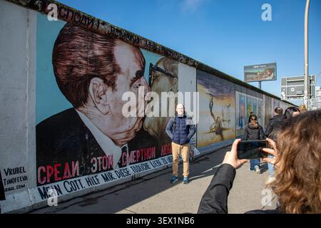 Touristen posieren für ein Foto neben Dmitry Vrubels berühmtem Wandgemälde auf einem erhaltenen Teil der Berliner Mauer in der East Side Gallery, Berlin, Deutschland Stockfoto