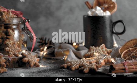 Ein gemütliches, festliches Stillleben mit schneeflockenförmigen Lebkuchenkeksen in einem Glasgefäß und auf einer rustikalen Oberfläche, gepaart mit einem dunklen Becher Kakao topp Stockfoto