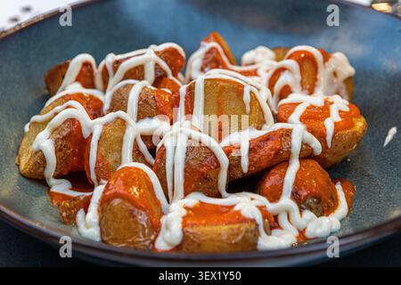 Spanien. Patatas Bravas, gebratene Kartoffelscheiben mit scharfer brava-Sauce und Knoblauch-Aioli, eine klassische Tapa, die auf einer dunklen Keramikplatte serviert wird Stockfoto