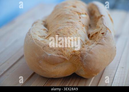 Frisch gebackener rustikaler Brotlaib auf einem Holztisch mit geringer Schärfentiefe. Traditionelles Backwarenprodukt mit goldener Kruste, Stockfoto