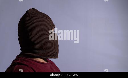 Seitenansicht eines erwachsenen Mannes mit braunem Strickbalaclava und einem kastanienbraunen Hemd, der direkt zur rechten Seite des Rahmens zeigt. Ein Auge ist teilweise VI Stockfoto