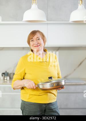 Fröhliche Seniorin, die in ihrer Küche lächelnd kocht Stockfoto