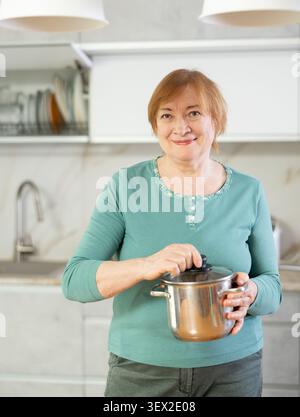 Glückliche reife Frau, die in ihrer Küche kocht, mit strahlendem Lächeln Stockfoto