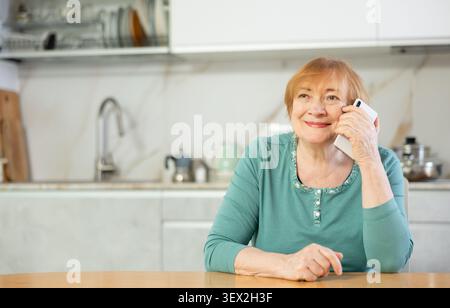 Fröhliche Seniorin, die in ihrer Küche telefoniert Stockfoto