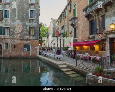 Venedig, Italien - 29. Mai 2026: Bezaubernde Kanalszene von Venedig mit Speisen im Freien, historischen Gebäuden und Menschen, die abends die Atmosphäre genießen Stockfoto