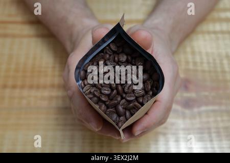 Nahaufnahme der Hände, die einen geöffneten Beutel mit frisch gerösteten Kaffeebohnen halten. Frischer Kaffeespezialitäten zum Mahlen und Brühen. Stockfoto