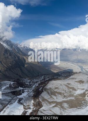 Blick aus der Vogelperspektive auf das Chunda-Tal mit schneebedeckten Berghängen, einem gewundenen Flusstal und dramatischen Wolken unter einem klaren blauen Himmel in Skardu, Gil Stockfoto