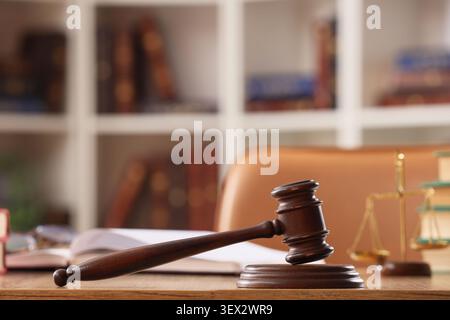 Hölzerner Hammer auf dem Schreibtisch mit Gesetzbüchern und Waagen Stockfoto