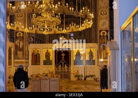 Das ruhige Innere einer orthodoxen Kirche im Gebet. Goldene Ikonen, prachtvoller Kronleuchter, Wände mit Fresken, treue Menschen. Stockfoto