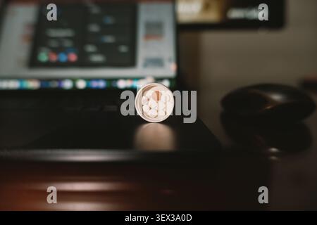 Nahaufnahme einer Münze mit kreisförmigen Ausschnitten auf einer Laptop-Tastatur in einem schwach beleuchteten Heimbüro, Stockfoto