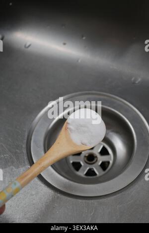 Backpulver auf einem Holzlöffel neben dem Abfluss des Küchenwaschbeckens Stockfoto