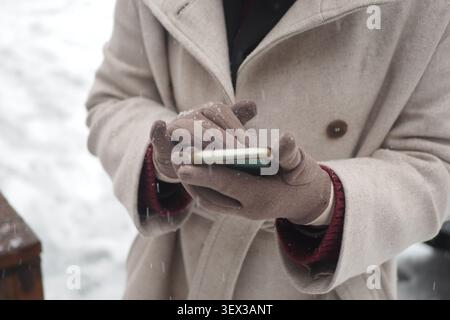 Die Person benutzt das Telefon, während sie im Schnee steht Stockfoto