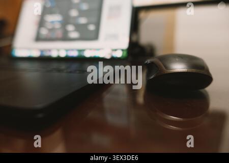 Nahaufnahme einer eleganten schwarzen Computermaus und eines Laptops auf einem polierten Holztisch im modernen Home Office, Stockfoto