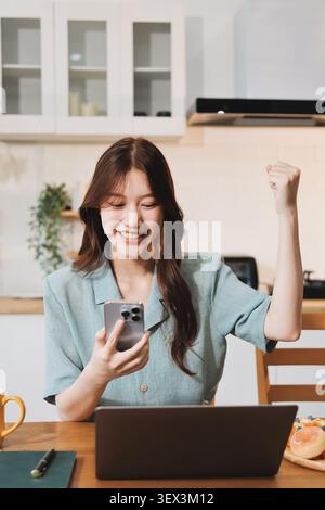Glück Unternehmer schönes Geschäft asiatische junge Frau tragen lässig Handy zum Einkaufen online genießen Sie mit sozialen Medien und Laptop zu Hause Stockfoto