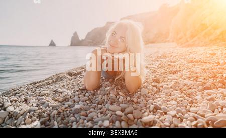 Frau Strandentspannung lächelnde blonde Frau, die am Kieselstrand liegt und während der goldenen Sommerferien wegblickt Stockfoto