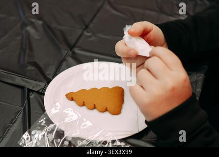 Kind dekoriert Lebkuchenbäumekse mit Glasur während der weihnachtsfeiertage Backaktivität Stockfoto