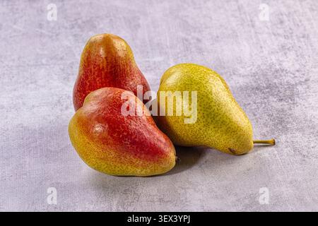 Drei reife Birnen mit rot-gelber Haut auf strukturierter grauer Steinoberfläche. Gesunde Fruchtkomposition mit natürlichem Licht, lebendigen Farben. Frisch o Stockfoto