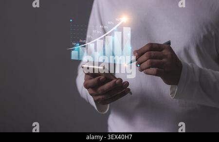 Junger Mann mit Smartphone zur Visualisierung des Geldwachstums auf dem Bildschirm des Telefons werden Diagramme und Diagramme angezeigt, die steigende Investitions- und Einsparungstrends zeigen Stockfoto