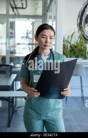 Langhaarige asiatische Ärztin mit Röntgenbefunden in den Händen Stockfoto