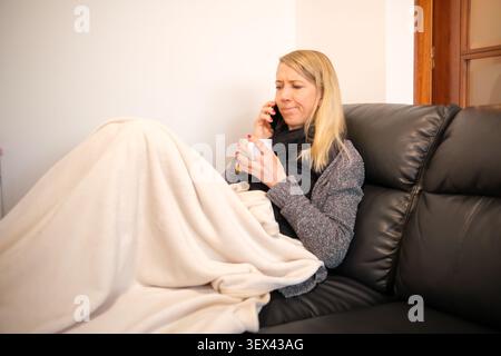 Die Frau, die mit einer Decke bedeckt ist, fühlt sich unwohl, während sie mit ihrem Handy spricht Stockfoto