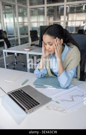 Müde gemischte Geschäftsfrau, die an Kopfschmerzen leidet Stockfoto