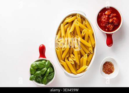 Ungekochte Penne-Pasta in weißer Auflaufform mit frischer Basilikum-Tomatensauce und Gewürz auf sauberem weißem Hintergrund Stockfoto