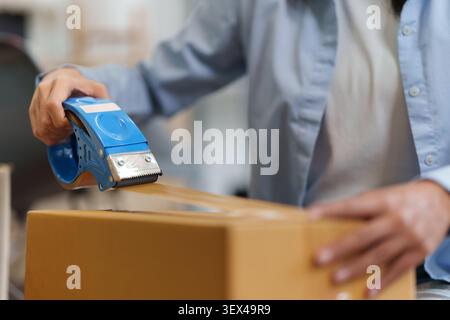 Abgeschnittene Hände, die Kartonschachtel mit Klebebandspender für den E-Commerce-Geschäftsversand verschließen Stockfoto