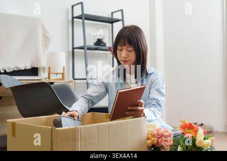 Asiatische Frau, die Pappschachtel mit Notizbuch in einem neuen Zuhause auspackt Stockfoto