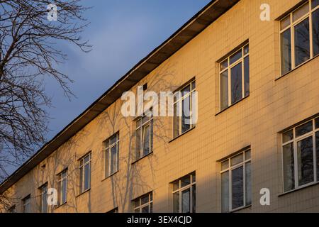 Diese strukturierte Fassade eines Büro- oder Schulgebäudes verfügt über einheitliche Fensterreihen, die während des Sonnenuntergangs erfasst werden, um warmes Licht, tiefe Schatten, A hervorzuheben Stockfoto