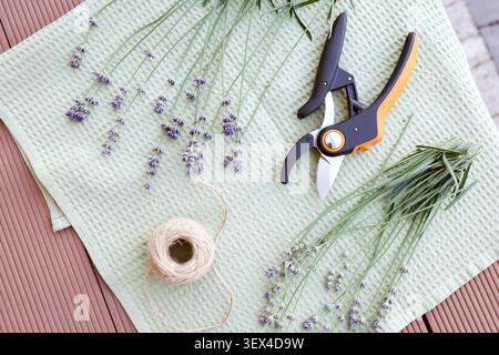 Lavendelstrauß-Bastelprozess auf hellgrünem Textilhandtuchhintergrund flache Lagenzusammensetzung. Bio-violette Blumen Garn Ball Gartenentaster Werkzeug Stockfoto