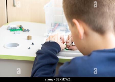Kiew, Ukraine - 21. März 2026: Das Kind konzentriert sich zutiefst auf Baustrukturen mit ineinander greifenden Kunststoffblöcken, was fantasievolle pla hervorhebt Stockfoto