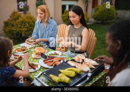 Multi-ethnische Freunde und Familie genießen eine Sommergartenparty mit gegrilltem Essen Stockfoto