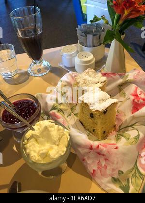 Eine gemütliche Brunch-Szene mit frischen Scones mit Zucker, Gläsern mit Beerenmarmelade und Sahne in einer gemütlichen Café-Umgebung. Stockfoto
