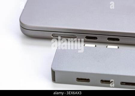 Nahaufnahme eines silbernen USB-Typ-C-Hub-Adapters aus Aluminium mit zwei Anschlüssen neben einem modernen Laptop mit Thunderbolt-Anschlüssen und SD-Karten-Slo Stockfoto