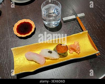 Eine exquisite Auswahl an frischem japanischem Nigiri-Sushi, serviert auf einer luxuriösen Goldplatte, begleitet von Ingwer, Sojasauce und Essstäbchen. Stockfoto