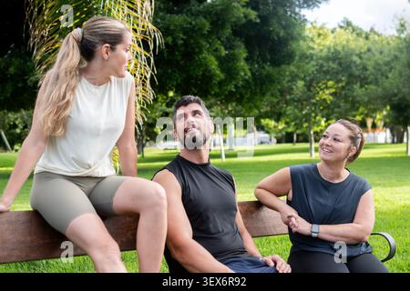 Drei aktive Freunde, die sich nach dem Training im Freien auf einer Parkbank unterhalten und entspannen. Stockfoto