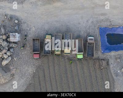 Aus der Vogelperspektive eines Sand- und Steinbruchs mit mehreren hintereinander geparkten Müllwagen, einer blauen Plane über einer Wassergrube und einem Arbeiter, der in der Nähe in einem Mann steht Stockfoto