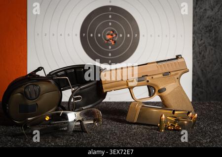 Schießstand-Trainingsset mit halbautomatischer Pistole, Gehörschutz, Schutzbrille, Munition und einem Papierziel mit Einschusslöchern. Stockfoto