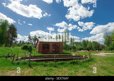 Historische Eisenbahndrehscheibe am alten Bahnhofsbahnhof Porvoo in Finnland. Im Hintergrund steht ein rustikales, rotes Backsteinmotorenhaus, umgeben von Grün Stockfoto